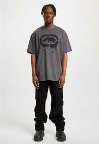 Gray oversized t-shirt with a black graphic print featuring a rhinoceros, paired with black cargo pants and chunky black boots.