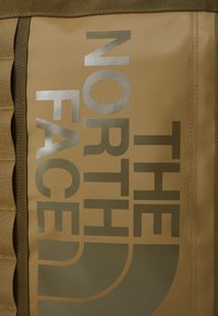 Brązowa torba z srebrnym logo "THE NORTH FACE" i okrągłym emblematem. Posiada zróżnicowaną teksturę i wzmocnione szwy.