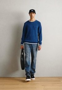 Blå genser med hvit kant, denimjeans, svarte sneakers og en svart veske. Enkel design, avslappet passform og glatte teksturer.