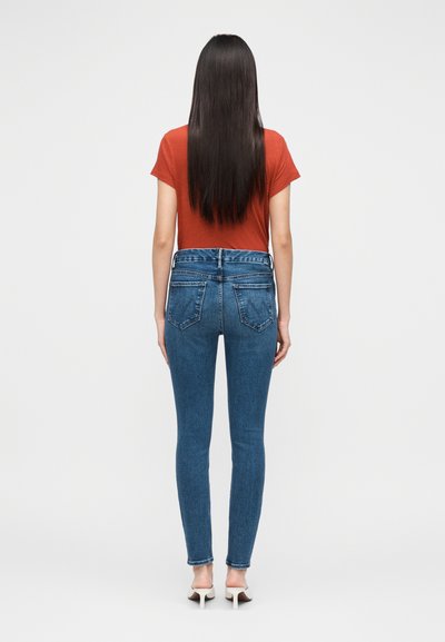 Tumedas sinised denimpüksid, millel on kõrge vöökoht, viis taskut ja veidi veniv materjal. Ühildatud roostepunase t-särgiga.