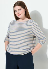 Beige gestreiftes Langarmoberteil mit blauen horizontalen Linien, lockere Passform, runder Ausschnitt, weicher Stoff, kombiniert mit marineblauen Hosen.