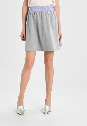 Grauer Baumwollrock mit einem gerafften, helllila elastischen Bund, der eine ausgestellte Silhouette und eine glatte Textur aufweist. Kombiniert mit silbernen High Heels.