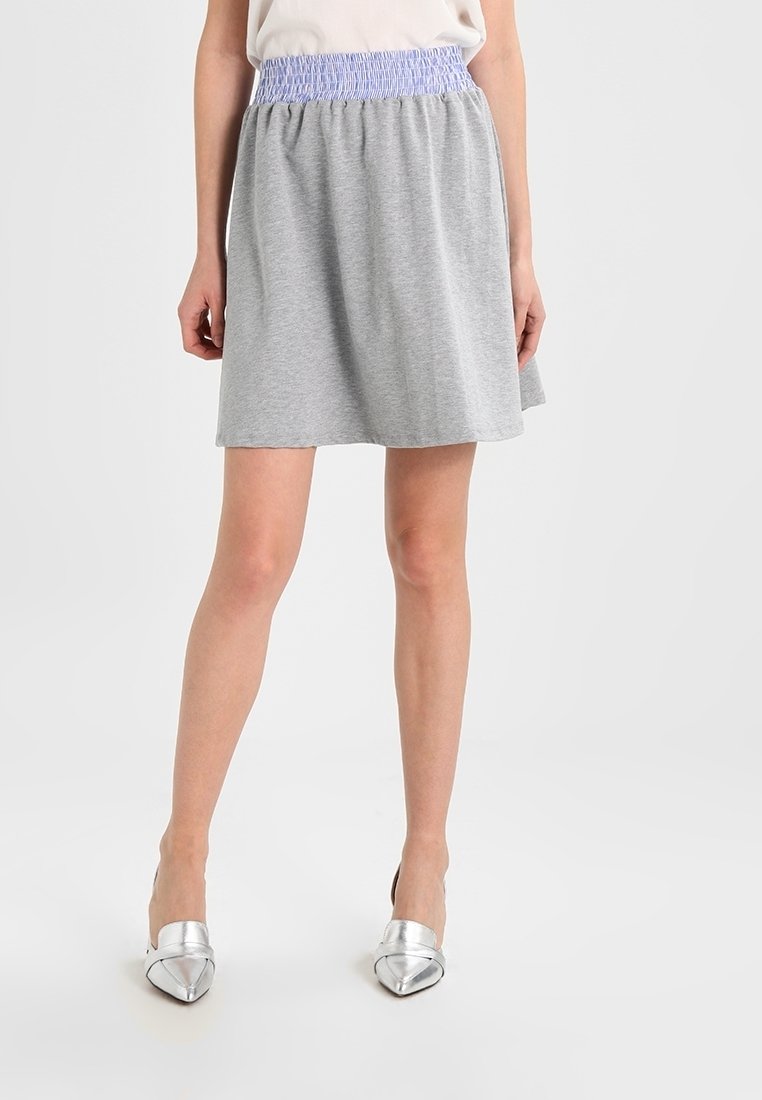 Falda de algodón gris con una cinta elástica de color púrpura claro fruncida en la cintura, que presenta una silueta acampanada y una textura suave. Combinada con tacones plateados.
