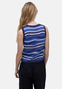 Top sin mangas de punto con patrones de olas en azul, blanco y marino; tela texturizada; escote con forma de concha; longitud corta, combinado con pantalones negros.