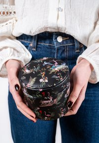 Round, black leather container with a floral and animal print, featuring a smooth texture and a fitted lid. Held by hands.