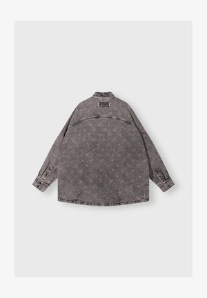 Grijze denimjas met een herhalend bloemenpatroon, knoopmanchetten, een kraag en een zichtbaar merklabel op de bovenrug.