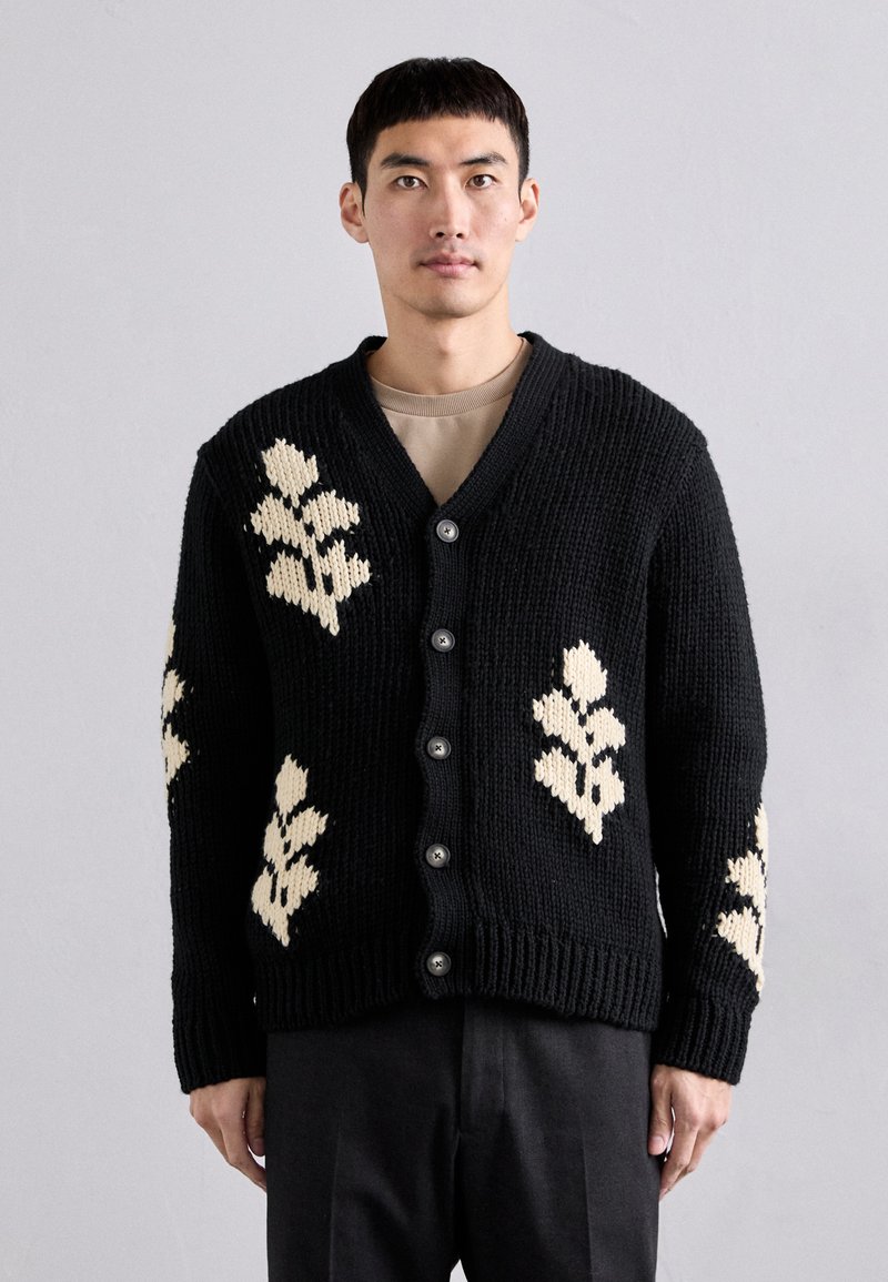 Sort strikket cardigan med cremefarvede blomster mønstre. V-udskæring med knapper foran samt rib-strikkede manchetter og kant.