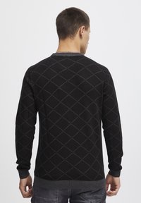 Schwarzer Pullover mit Rautenmuster in grauem Garn. Gerippter Kragen und Bündchen. Lange Ärmel. Der Stoff hat eine glatte und weiche Textur.