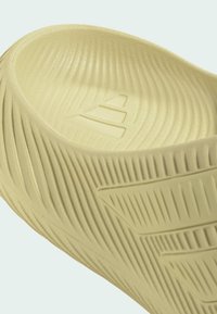 Beige slip-on sandal med teksturerede riller og geometriske mønstre på sålen og øverste kant.