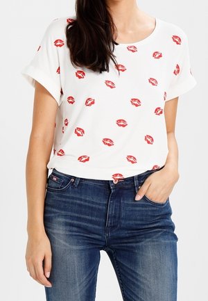 Valkoinen, lyhythihainen t-paita, jossa on punaisen huulipunan suukkojen kuviot, yhdistetty keskisinisiin farkkuihin, joissa on klassinen istuvuus ja pehmeä kangas.