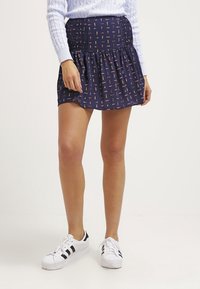 Geprinte marineblauwe rok met een elastische tailleband en een uitlopende onderkant, voorzien van kleurrijke verticale patronen. Gecombineerd met witte sneakers.