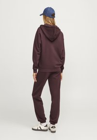 Felpa borgogna con pantaloni abbinati in un tessuto morbido, con cappuccio, polsini a costine e sneaker bianche con accenti neri e un logo.