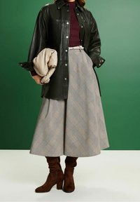 Olijfgroen leren shirt, bordeauxrood geribbeld topje, geruit A-lijn rok en bruine suède kniehoge laarzen. Inclusief een beige geplooide clutch.