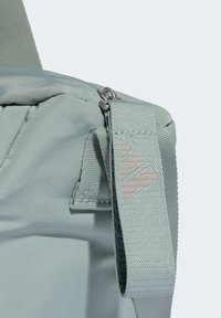 Lysegrøn rygsæk med lynlås, tekstureret stof og en fremtrædende strop med en grå logoaccent. Kompakt og slankt design.