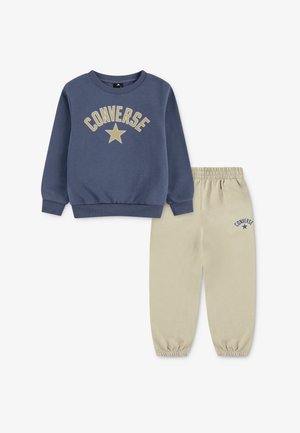 Sudadera azul marino con la inscripción "CONVERSE" y un gráfico de estrella; combinada con pantalones jogger beige con cintura elástica y el logo de "CONVERSE" en el lateral.