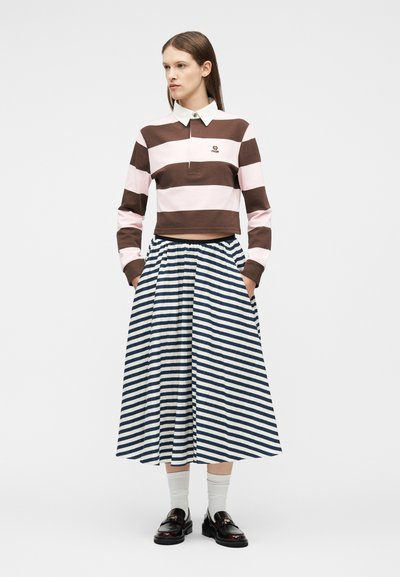 Γυναίκα που φοράει καφέ και ροζ ριγέ μακρυμάνικο πόλο, midi φούστα με ριγέ σε ναυτικό μπλε και λευκό, λευκές κάλτσες και μαύρα loafers.