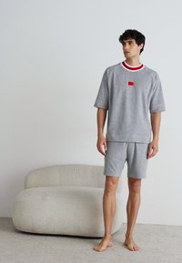 Graues, übergroßes T-Shirt aus Baumwolle mit roten und weißen Akzenten, kombiniert mit passenden Shorts. Lässige Passform, glatte Textur und schlichtes Design.