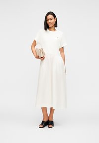 Λευκό midi φόρεμα με κοντά μανίκια και σούρα στη μέση, σε συνδυασμό με μαύρα mules ανοιχτής μύτης και μπεζ τσάντα χειρός. Λείο ύφασμα.