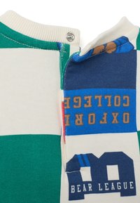 Polo en coton multicolore avec des rayures vertes et crème, présentant une patte bleue avec le texte "OXFORD" et "BEAR LEAGUE". Comprend une fermeture à pression.