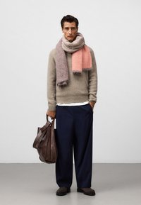 Jasno beżowy sweter z dzianiny, szaro-różowy szal, granatowe szerokie spodnie, brązowa skórzana torebka oraz ciemnoszare buty w minimalistycznym otoczeniu.