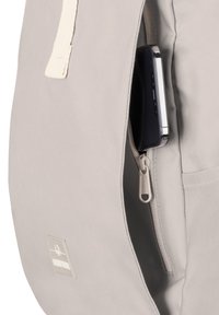 Gray backpack made of textured fabric, featuring a side zipper and a pocket holding a smartphone. Includes a simple logo patch.