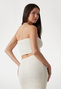 Ensemble en crochet blanc composé d'un top court sans bretelles et d'une jupe taille haute avec des motifs texturés et un bord festonné.