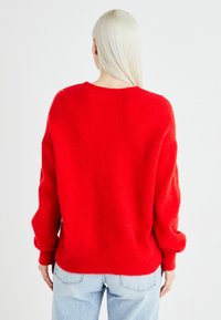 Pull rouge, fluffy avec une coupe ample, un col rond et des manches longues. Associé à un jean bleu clair, vu de dos.