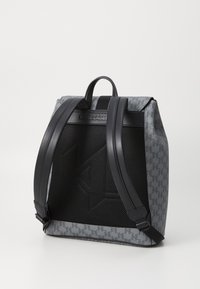 Sac à dos gris avec des sangles en cuir noir, doté d'un panneau en maille et d'un détail de logo. Forme rectangulaire avec un design structuré.