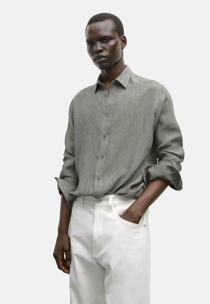 Light gray button-up shirt in a textured fabric, featuring rolled sleeves and a classic collar, paired with white high-waisted trousers.