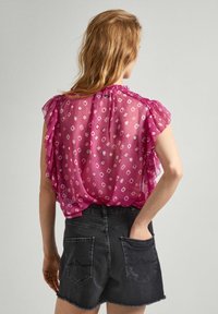 Sheer pink blouse with ruffled short sleeves, featuring a diamond pattern. Paired with high-waisted black denim shorts.