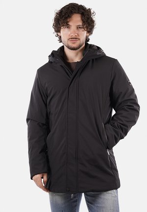 Parka nera impermeabile con cappuccio, dotata di una cerniera frontale, tasche laterali e una linea dritta. Texture liscia e design minimal.