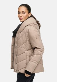 Veste matelassée beige avec capuche, présentant un détail de couture en diagonale et une fermeture à boutons-pression. Doublure intérieure noire et accents de col.