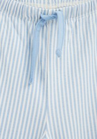 Gros plan d’un pantalon de pyjama en tissu rayé verticalement bleu clair et blanc, avec une taille élastique et un cordon bleu noué.