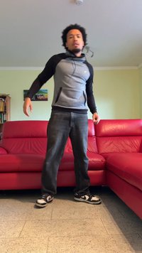 Un divano in pelle rossa con una texture liscia, accostato a una persona in una felpa sportiva grigia e nera e jeans neri, che si trova nei paraggi.