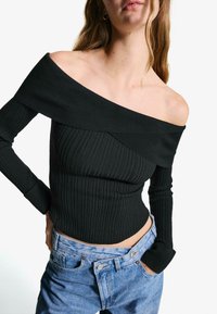 Black off-shoulder ribbed top with long sleeves, featuring a fitted design and horizontal texture, paired with high-waisted blue jeans.