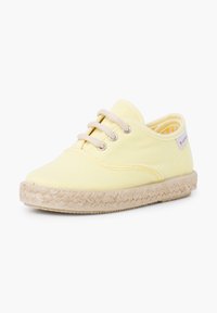 Chaussure en toile jaune avec semelle en caoutchouc et enroulement en jute. Dispose d'un design à lacets et d'œillets en métal. Intérieur doublé d'un motif à carreaux.