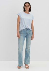 Top azzurro chiaro a maniche corte abbinato a jeans bootcut sbiaditi e sandali argentati; tessuto morbido, vestibilità rilassata, dettagli annodati sottili davanti.