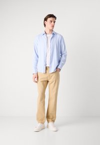 Cămașă albastră deschisă cu nasturi, tricou alb, pantaloni bej și adidași albi. Texturile materialelor sunt vizibile; cămașa are o croială lejeră și un model ușor.
