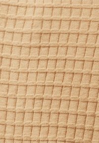 Texturovaná tkanina v světle béžové barvě, se vzorem mřížky vytvořeným vyvýšenými čtverci, což vytváří hmatový, tkaný vzhled.