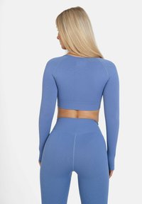 Blaues langärmeliges Crop-Top und hochtaillierte Leggings aus einem strukturierten, dehnbaren Stoff, mit einer figurschmeichelnden Passform und nahtloser Verarbeitung.