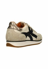 Sneaker met een beige leren bovenkant, zwarte zigzagaccenten en een zilveren metalen hiel. Textuur van suède en rubberen zool zorgen voor contrast.