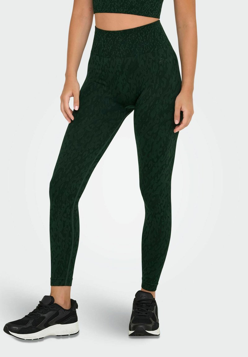 Leggings verde scuro con un delicato motivo a leopardato, vita alta, tessuto elasticizzato e abbinati a sneaker sportive nere.