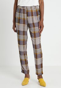 Randiga byxor i vitt, gult, lila och bruna mönster. Lättviktigt tyg, design med smal ben, elastisk midja, kombinerat med gula skor.