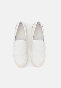 Scarpe bianche slip-on con un motivo geometrico testurizzato, caratterizzate da una parte superiore liscia, punta rotonda e sottili accenti dorati sui lati.