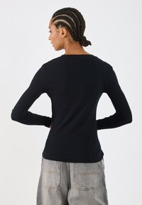 Črn dolg rokav majica iz rebraste tkanine, s krožnim izrezom, v oprijetem kroju, kombinirana z svetlo sivo visokim pasom denim hlačami.