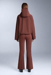 Barna, testhez simuló dzseki magas gallérral és bő szárú nadrág, sima anyagból készült. Mindkét darabon látható varrásdíszítések találhatók.