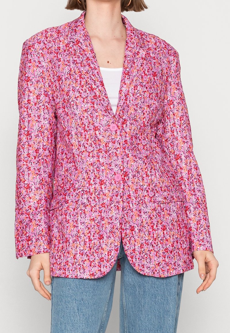 Blazer rose à motif floral en tissu texturé, doté de deux boutons, de revers crantés et de deux poches avant, avec un motif vibrant de plusieurs couleurs.