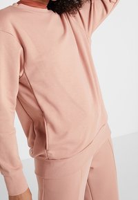 Sweatshirt crewneck rose clair en tissu doux, avec des manches longues, des poignets côtelés et une coupe décontractée.
