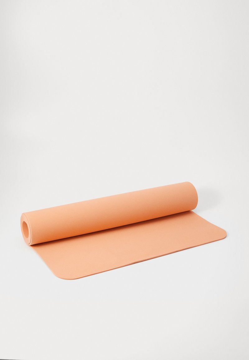 Tapete de ioga em pêssego, parcialmente desenrolado, feito de material texturizado, com bordas arredondadas e uma superfície suave. Design durável e flexível.