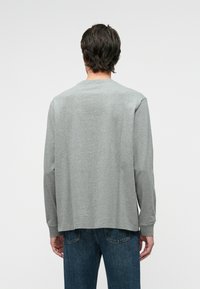 Γκρίζο μπλουζάκι μακρυμάνικο με στρογγυλή λαιμόκοψη και επίπεδες ραφές, συνδυασμένο με μπλε τζιν παντελόνι. Μαλακό ύφασμα, μίνιμαλ σχέδιο και άνετη εφαρμογή.